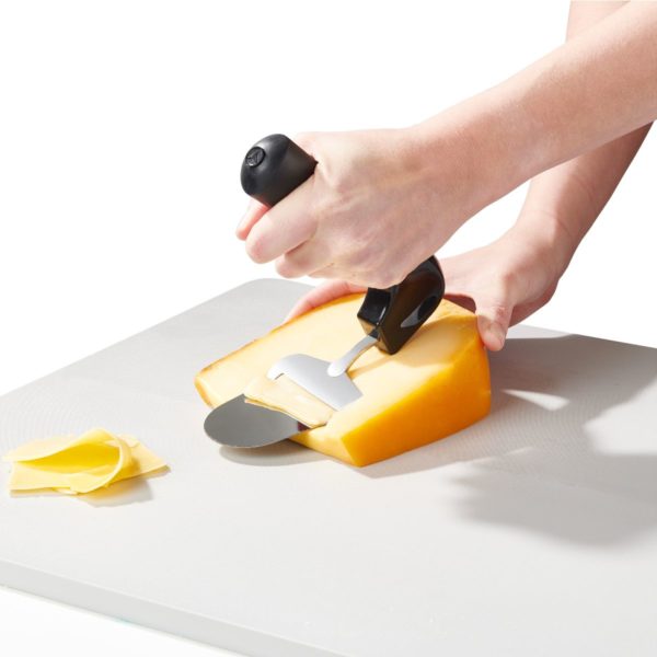 Juustohöylä ergonominen ei rasita rannetta. Käyttökuva juuston leikkaamisesta.